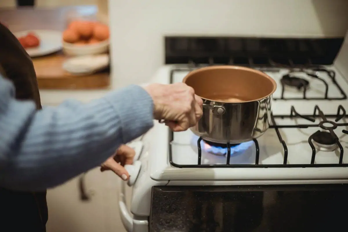 Crop unrecognizable housewife placing saucepan on burning stove