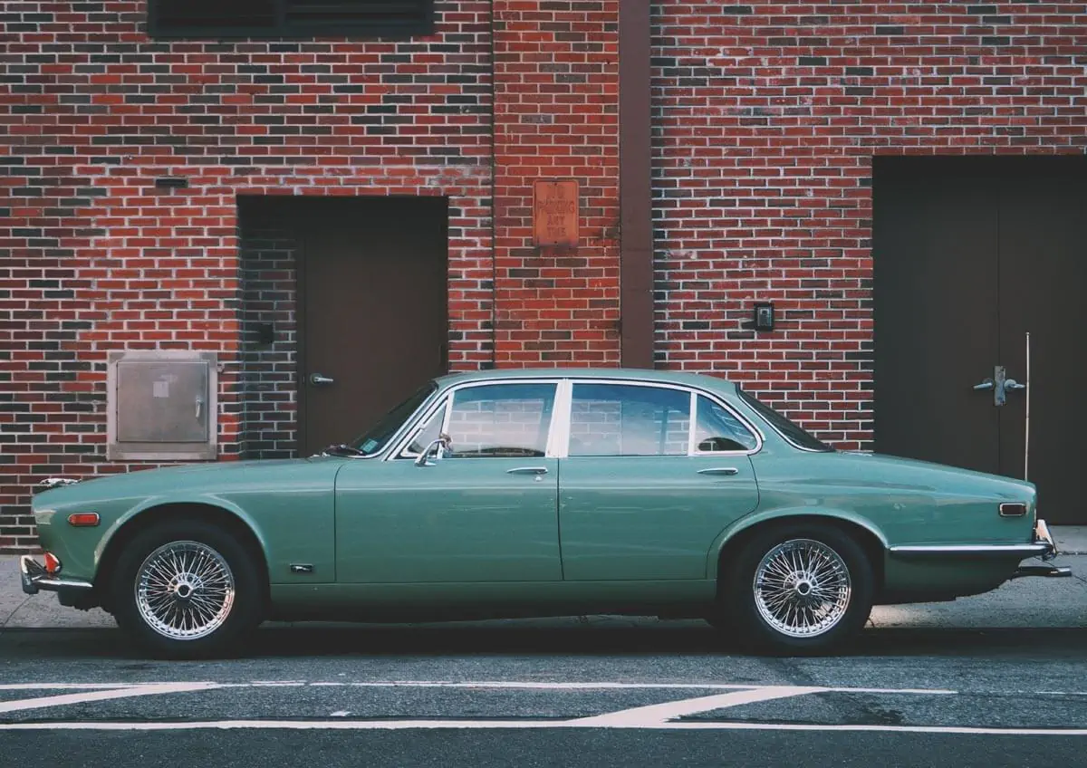 A classic green car is parked in front of a brick building