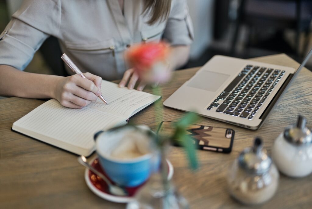 person-writing-on-a-notebook-beside-macbook