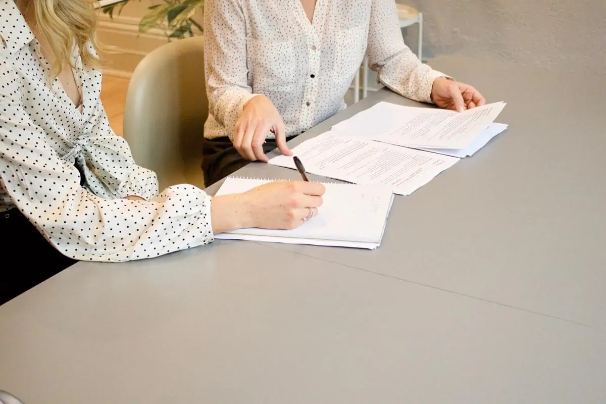 woman signing on white printer paper beside woman