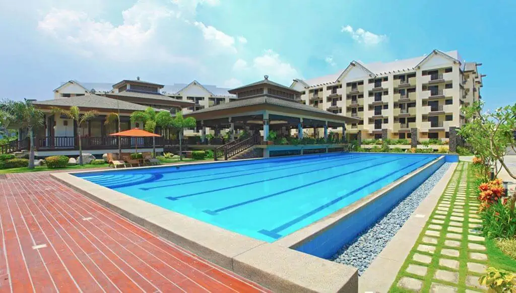 Swimming pool next to a clubhouse, condo units, and a small garden during the day