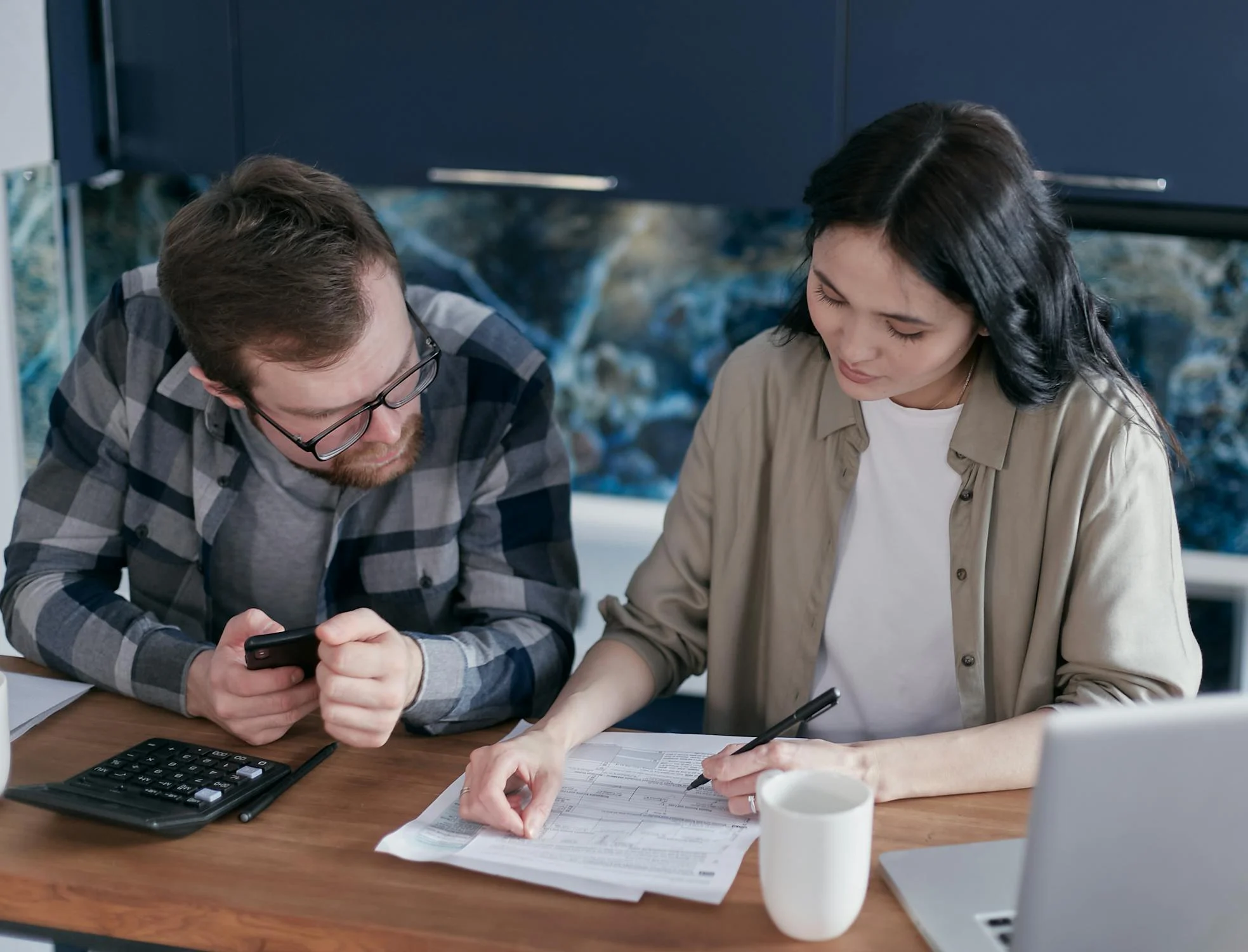 man holding a cellphone sitting beside the woman signing documents