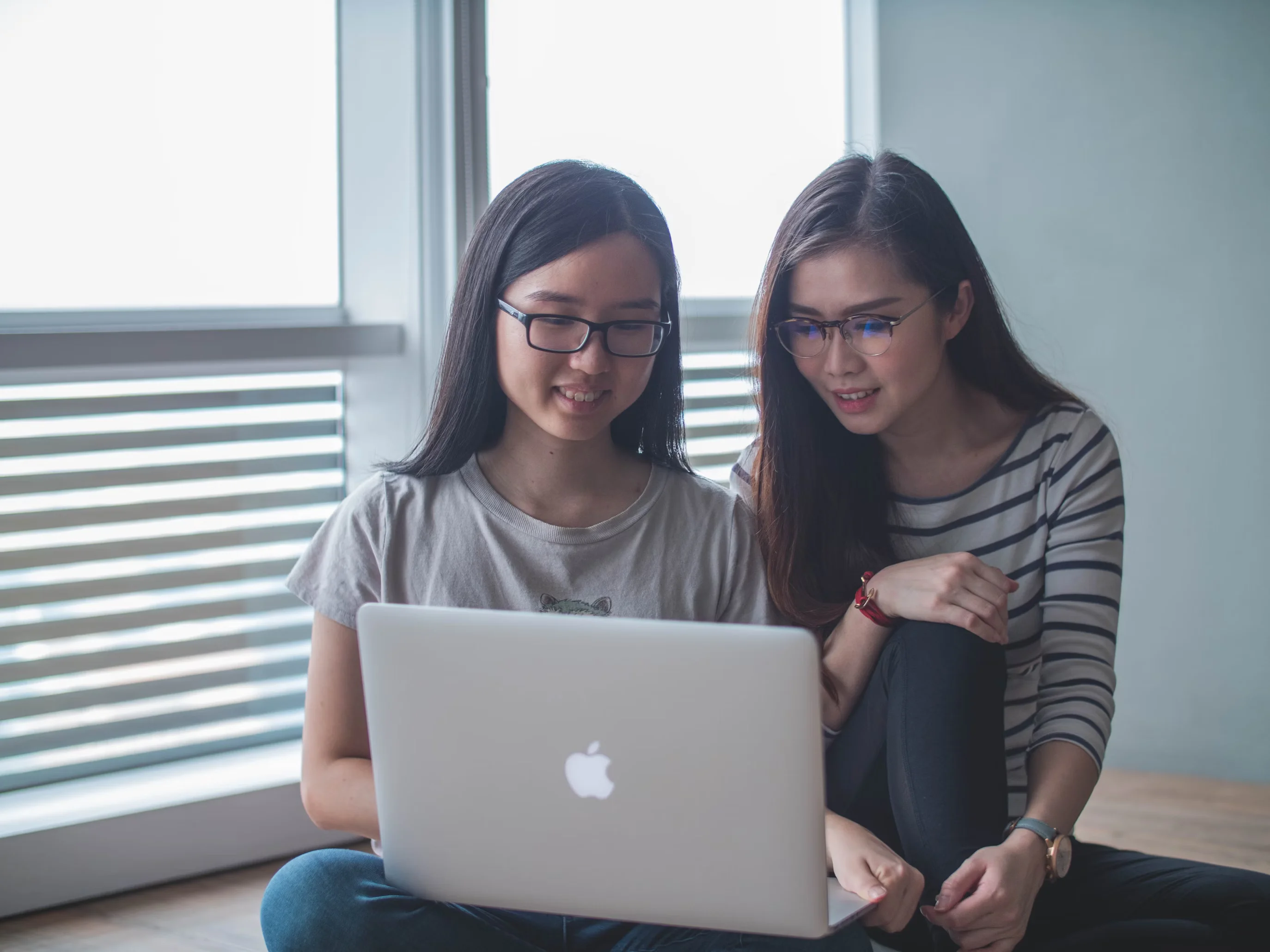 two smiling women staring on silver mac book