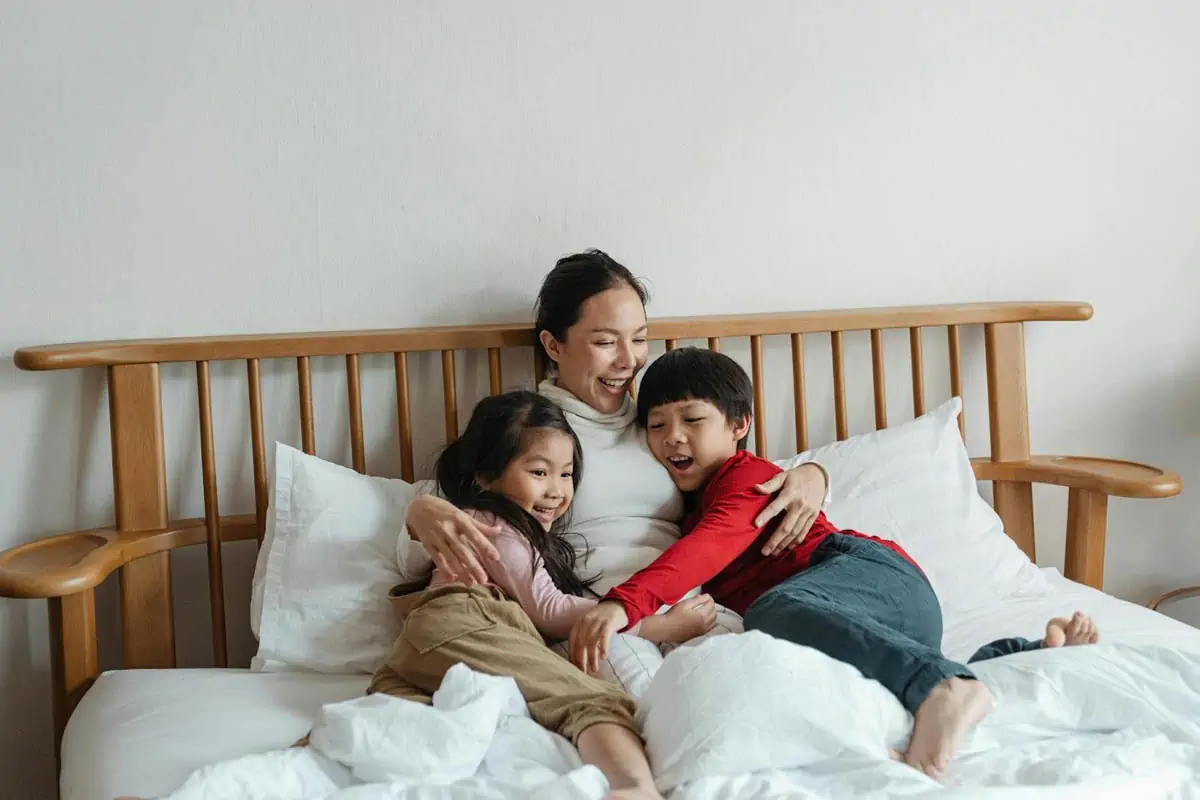 cheerful-ethnic-mother-hugging-children-lying-in-bed