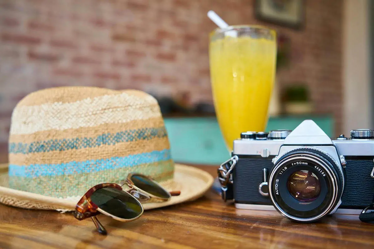 gray-and-black-dslr-camera-beside-sun-hat-and-sunglasses